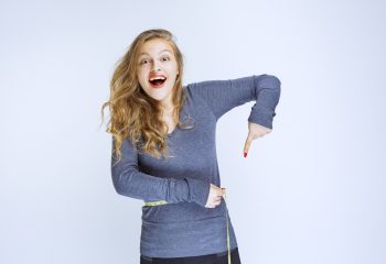 Blonde girl pointing at her waist size. High quality photo