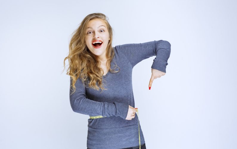 Blonde girl pointing at her waist size. High quality photo