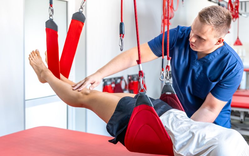 Doctor physiotherapist rehabilitologist next to a female patient lying on a couch in the office.