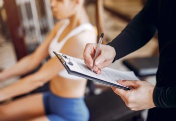 Couple in the gym. A woman performs exercises. Man in a black t-shirt